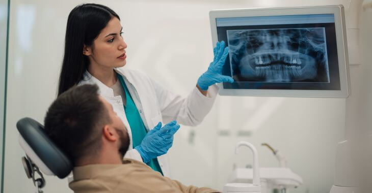A dentist showing a dental imaging and explaining the issue to a man sitting in a dental chair
