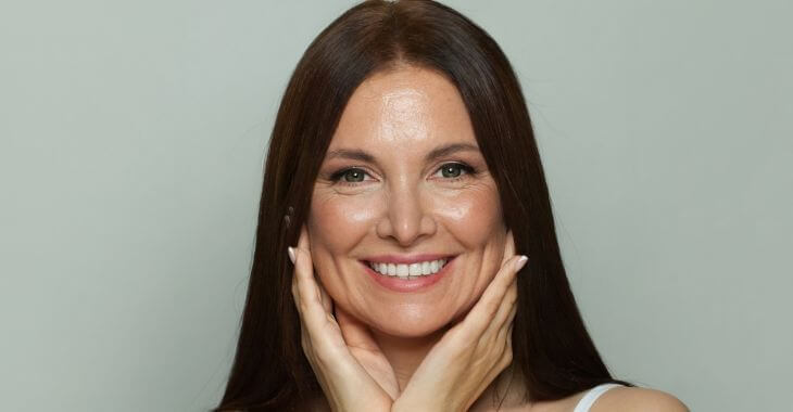 Mature youngish looking woman with a perfect smile touching her jawline