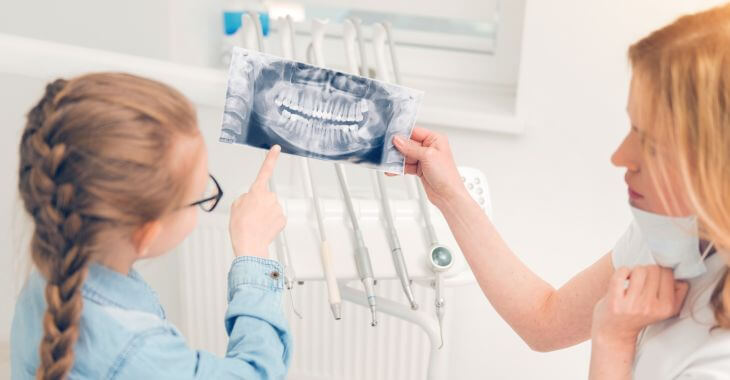 A dentist showing a dental x-ray to a girl with tooth issue sitting in a dental chair