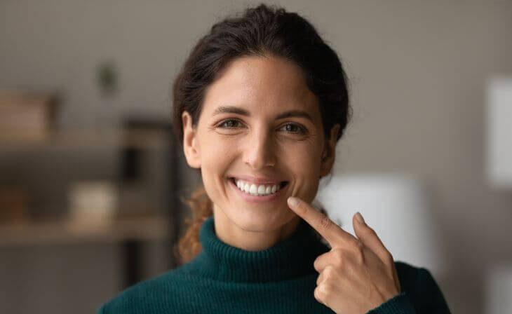Smiling woman with beautiful smile pointing at her tooth