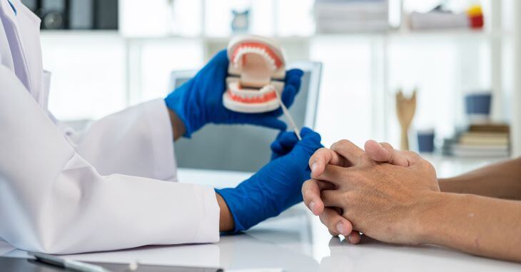 Orthodontist explaining a male patient proper bite alignment on a dental model